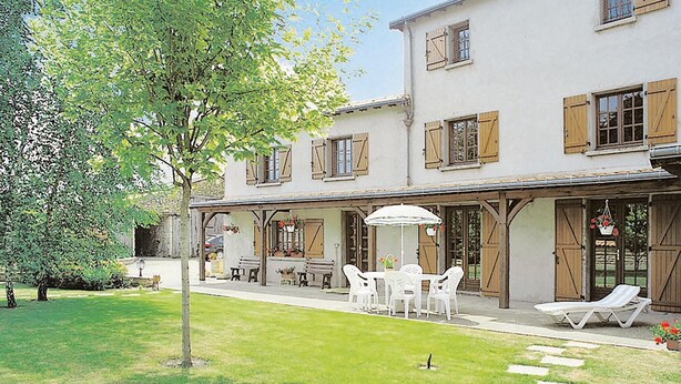 Un edificio a due piani con un portico coperto, dotato di posti a sedere all'aperto e un tavolo con ombrellone bianco.