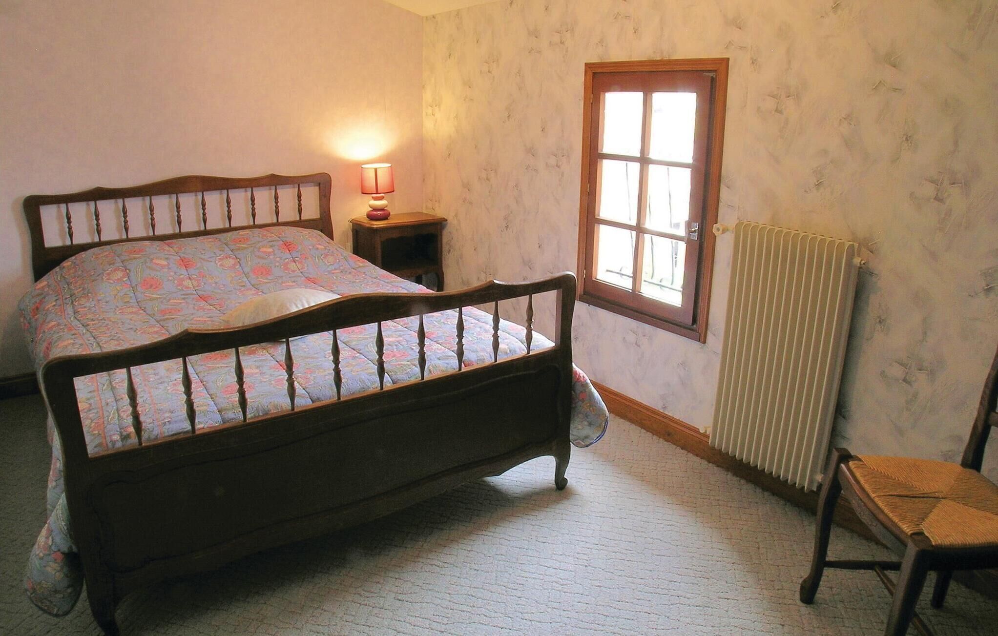 A bedroom with a wooden bed, a nightstand with a lamp, a radiator, and a window.