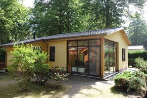 En moderne, gul bygning med store glasfacader, en overdækket terrasse og en have.