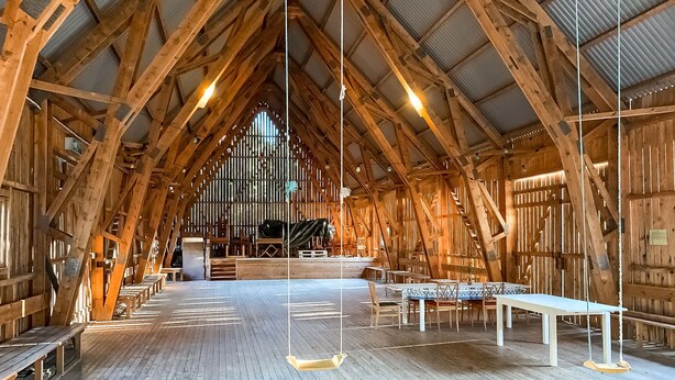 A spacious wooden hall with high ceilings and a central altar, featuring benches and tables for seating.