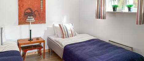 Une chambre avec deux lits simples, une table de chevet, une lampe, un tapis rouge et une fenêtre avec des rideaux.