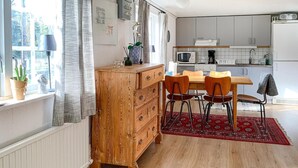 A compact kitchen with wooden cabinets, a dining table with chairs, and a red rug.