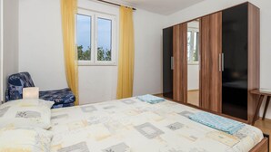 A bedroom with a bed, a chair, a wardrobe, and a window with curtains.