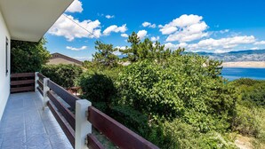 A balcony with a view of a coastal landscape, including trees and a distant shoreline.