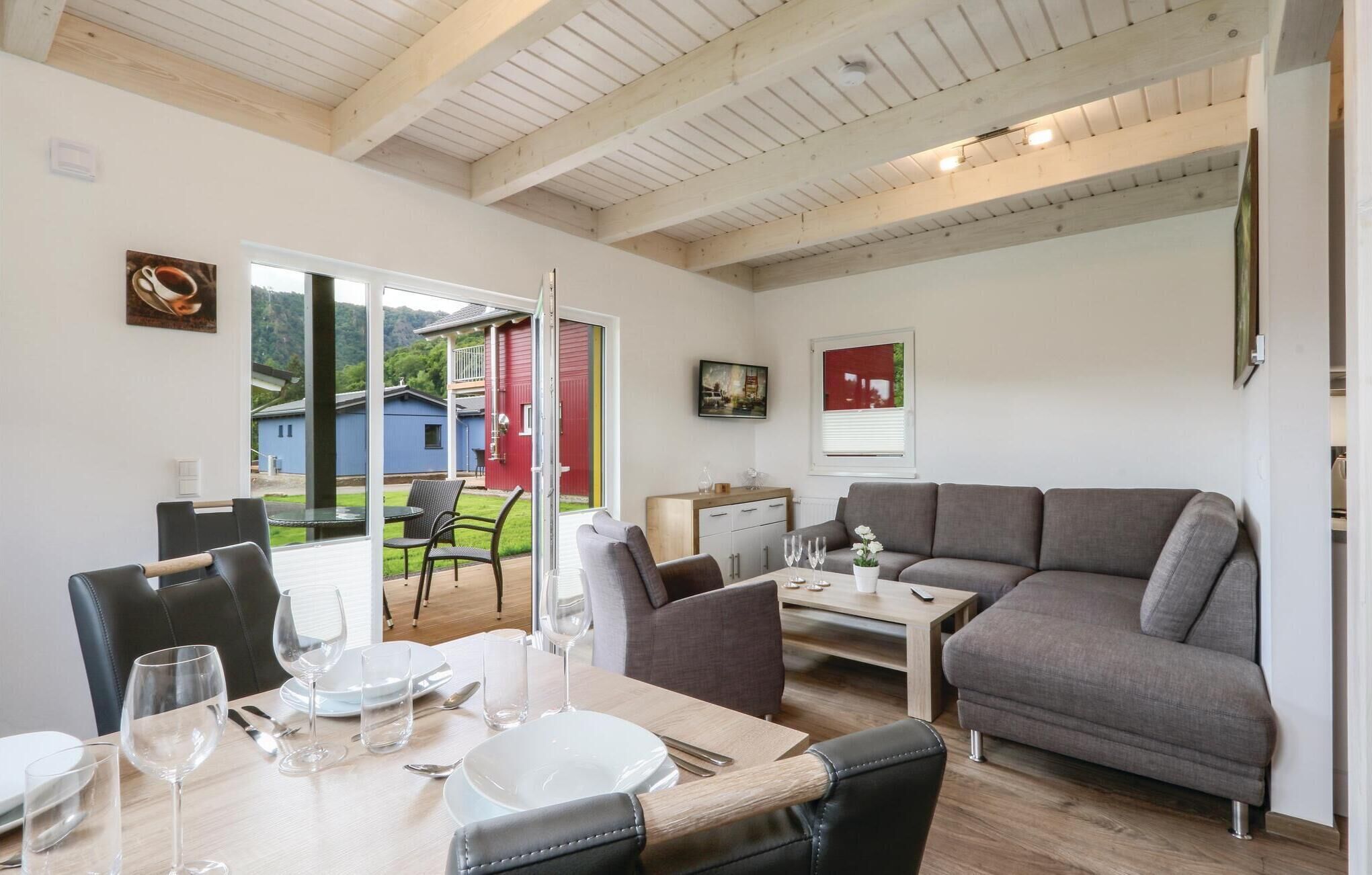 Ein modernes Wohnzimmer mit einem grauen Sofa, einem Esstisch für vier Personen und einer roten Tür, die nach draußen führt.