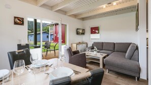 Un salon moderne avec un canapé gris, une table à manger pour quatre personnes et une porte rouge donnant sur l’extérieur.