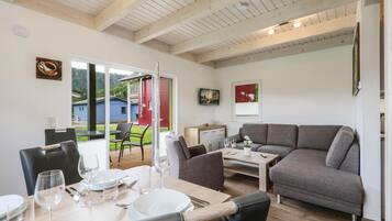 Ein modernes Wohnzimmer mit einem grauen Sofa, einem Esstisch für vier Personen und einer roten Tür, die nach draußen führt.