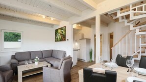 Un salon moderne avec un canapé d’angle gris, une petite table basse et un coin repas avec une table en bois mise pour un repas.