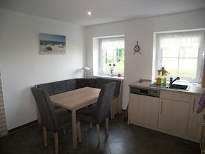 A compact kitchen with a dining area, a clock on the wall, and a window with a view of greenery.