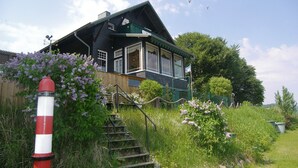 Een huis met een wenteltrap naar een veranda, omringd door begroeiing en een vlag.