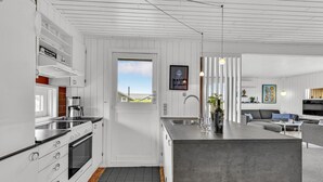 Et moderne køkken med indbygget ovn, kaffemaskine og en stor ø med vask.