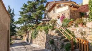 A narrow stone pathway leading to a stone building with a wooden staircase and a metal railing.