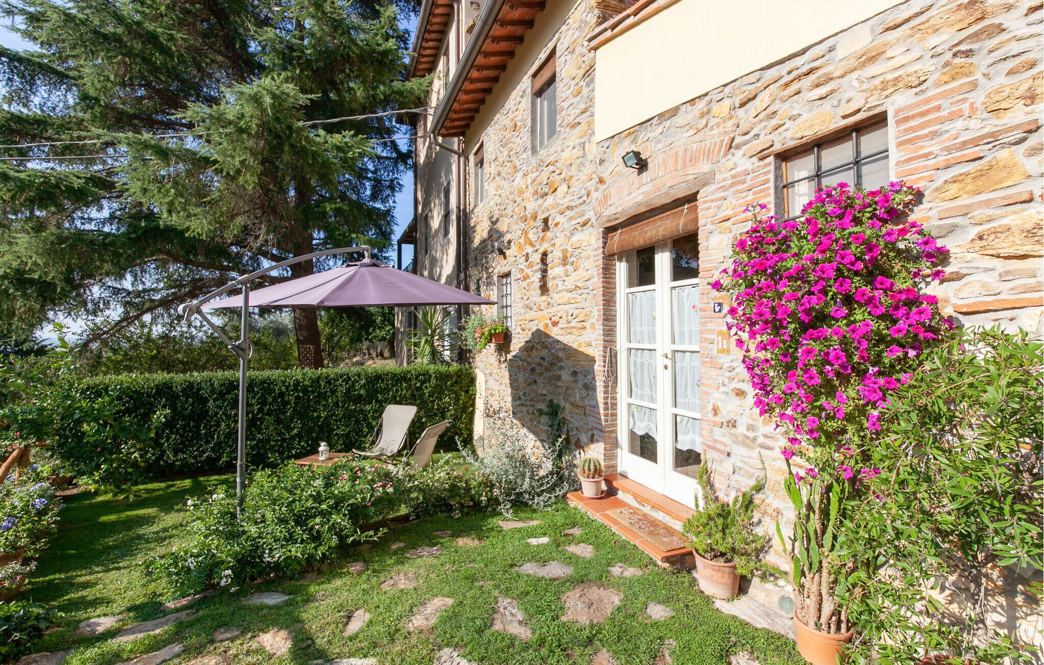 Un edificio de piedra con jardín, un patio con mesa y sillas, y una maceta colgante.