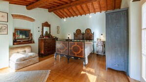 A bedroom with wooden flooring, a bed with a wooden headboard, a dresser, a bench, and a wardrobe.