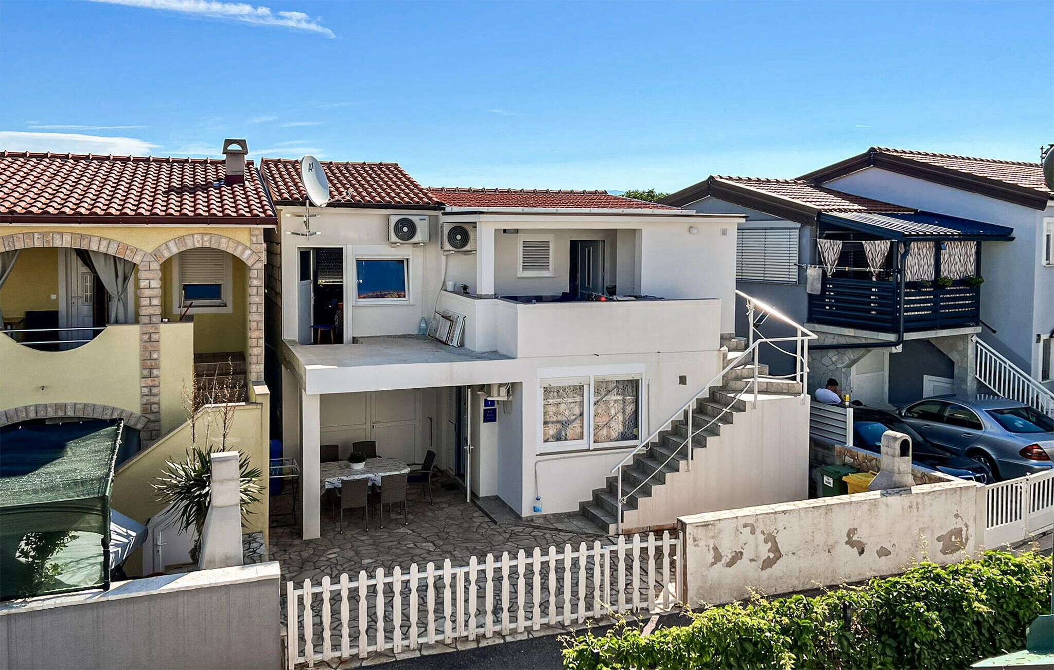 Ein zweistöckiges Haus mit Balkon und Treppe, ein Auto ist vor der Tür geparkt.