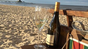 A bottle of wine and two glasses on a wooden board on a sandy beach with a pier in the background. - Residence Bismarck App. Maris (Heringsdorf)