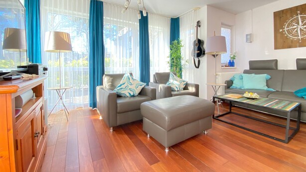 A modern living room with a sofa, ottoman, coffee table, and a guitar wall decoration. - Residence Bismarck App. Maris (Heringsdorf)