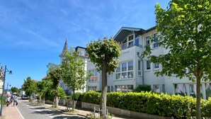 A street lined with multi-story buildings, a clear sky, and a sidewalk with trees and a hedge. - Residence Bismarck App. Maris (Heringsdorf)