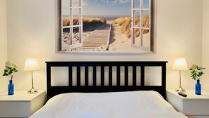 A bedroom with a large window, a wooden headboard, two bedside tables with lamps, and a bed with a white bedspread. - Residence Bismarck App. Maris (Heringsdorf)