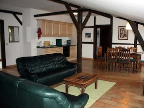 Un salon avec un canapé en cuir noir, une table basse en bois et un coin repas comprenant des chaises et une table en bois.