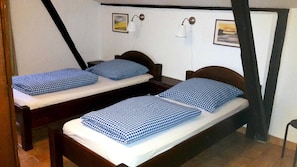 A room with two single beds, each with a checkered bedspread and matching pillows. There are two wall-mounted lamps and two framed pictures on the walls. - Apartment I - Apartments in a farmhouse - Property 44365 (Papendorf)