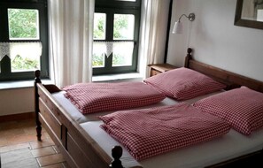 A room with two single beds, a nightstand, a window with curtains, and a wall-mounted lamp.