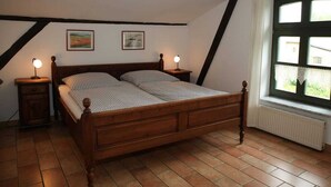 Une chambre à coucher avec un lit en bois, deux tables de chevet avec des lampes, un radiateur et deux tableaux encadrés accrochés au mur.