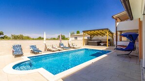 Une piscine avec des chaises longues et des parasols, un patio couvert et une vue sur le paysage environnant.