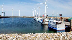 A harbor with boats docked, a rocky shoreline, and wind turbines in the background. - 3 bedroom nice home in Glesborg (Glesborg)