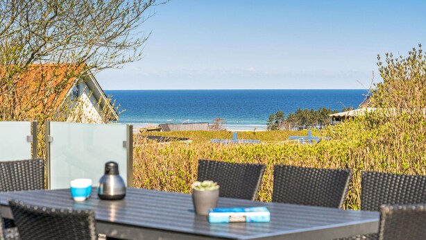 A dining area with a table and chairs overlooking a beach and ocean. - 3 bedroom nice home in Glesborg (Glesborg)