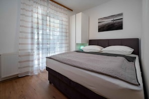Une chambre à coucher avec un lit, un radiateur, une fenêtre avec des rideaux et un tableau accroché au mur.