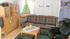 A cozy living room with a plaid sofa, a wooden cabinet, a small table with a lamp, and a television.
