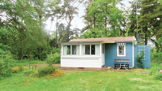A small, single-story cabin with a porch, surrounded by dense forest.