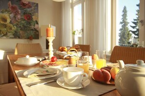A breakfast setting with a table set for two, including plates, cups, a teapot, and a fruit bowl.
