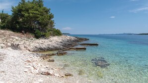 A rocky shoreline with clear turquoise water, a few scattered rocks, and a dense cluster of trees on the left. - Pet friendly home in Nova (Nova)
