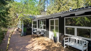 A wooden deck with a white bench, a table with chairs, and a potted plant. - Amazing home in Nexø with sauna (Nexø)