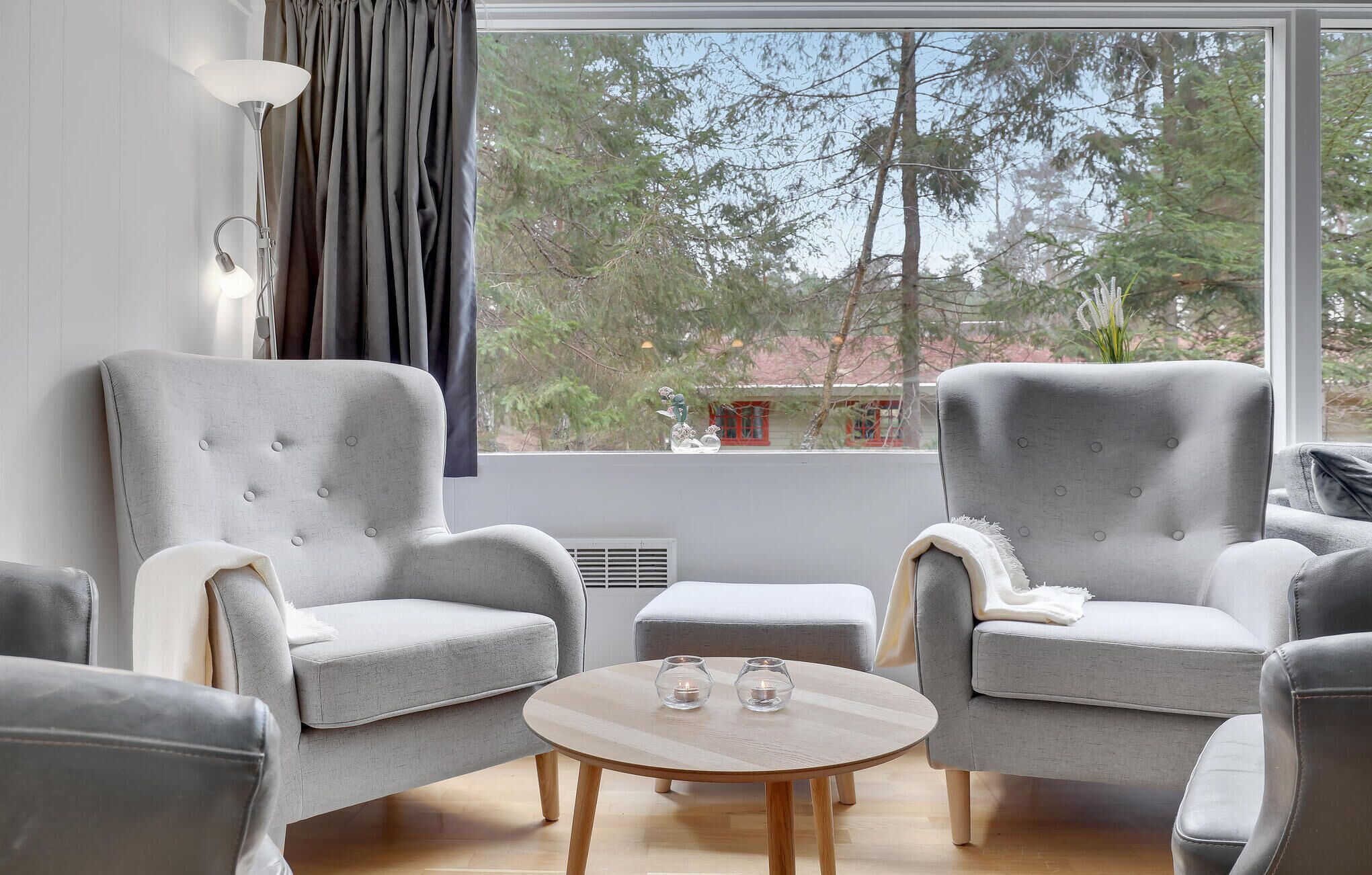 Ein modernes Wohnzimmer mit zwei grauen Sesseln, einem runden Couchtisch und Blick auf Bäume durch ein großes Fenster.