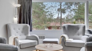 A modern living room with two grey armchairs, a round wooden coffee table, and a view of trees through a large window. - Amazing home in Nexø with sauna (Nexø)