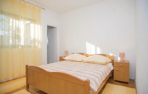 Ein Schlafzimmer mit einem hölzernen Bett, Nachttischen und einem Fenster mit durchscheinenden Vorhängen.