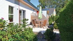 A house with a patio area featuring a table and chairs, surrounded by greenery and a wooden fence. - Beach front home in Süssau/Ostsee (Süssau/Ostsee)