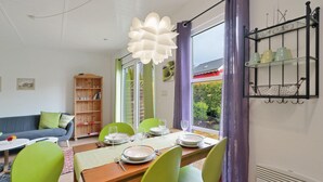 A dining area with a wooden table set for four, surrounded by green chairs, and a large window with purple curtains. - Beach front home in Süssau/Ostsee (Süssau/Ostsee)