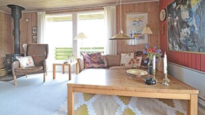 A cozy living room with a wooden table, a sofa, a chair, a fireplace, and a painting on the wall. - 4 bedroom gorgeous home in Fanø (Fanø)