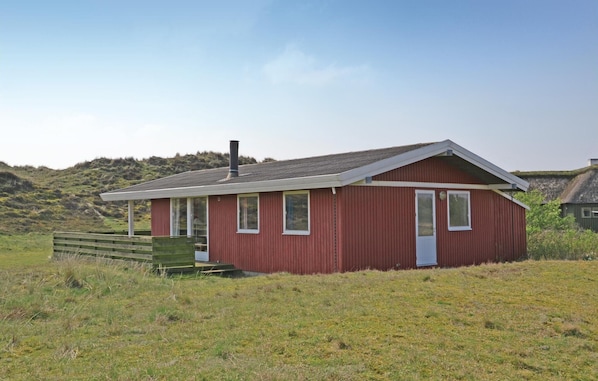 A small, single-story red building with a sloped roof, a chimney, and a wooden deck. - 4 bedroom gorgeous home in Fanø (Fanø)