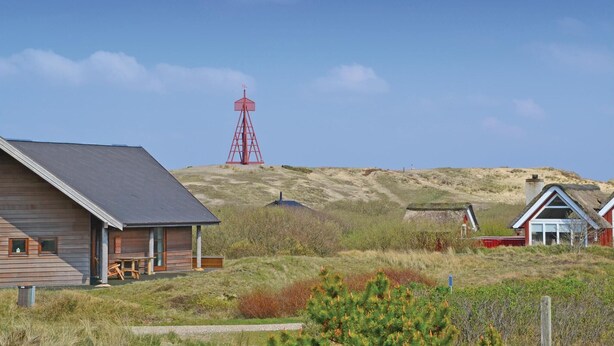 A wooden cabin with a sloped roof, a red windmill, and a thatched-roof house on a grassy hill. - 4 bedroom gorgeous home in Fanø (Fanø)