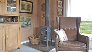 A cozy room with a large wooden cabinet, a brown leather chair, a vintage stove, and framed artwork on the walls. - 4 bedroom gorgeous home in Fanø (Fanø)