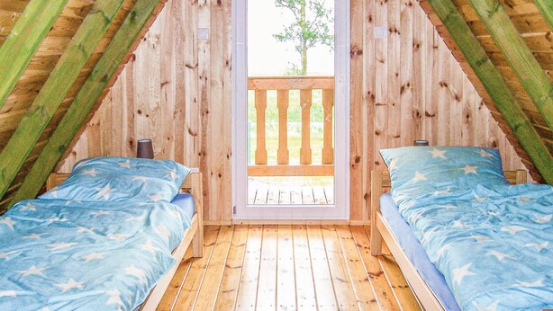 Un dormitorio rústico en el ático, con dos camas, piso de madera y vistas a través de una ventana con barandilla de madera.