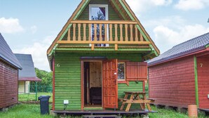Una cabaña de madera pequeña y verde con un balcón, una puerta y una mesa de picnic.