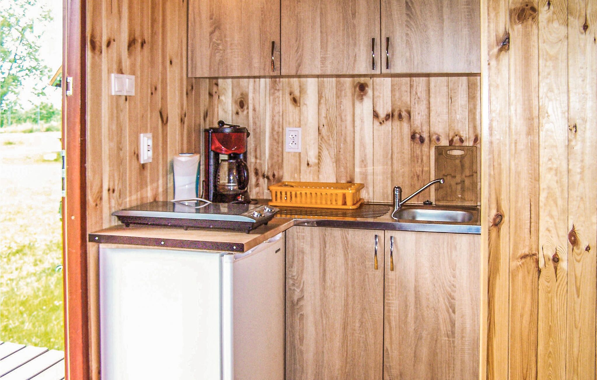 Eine kleine, hölzerne Küche mit Spüle, einer Kaffeemaschine und einem kleinen Kühlschrank.