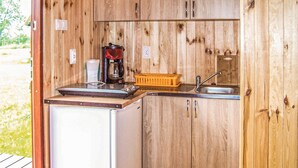 Una cocina de madera compacta con un lavamanos, una cafetera y un refrigerador pequeño.
