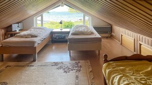 Ein gemütliches Schlafzimmer im Dachgeschoss mit zwei Einzelbetten, einem großen Fenster mit Meerblick und einer Holzbalkendecke.